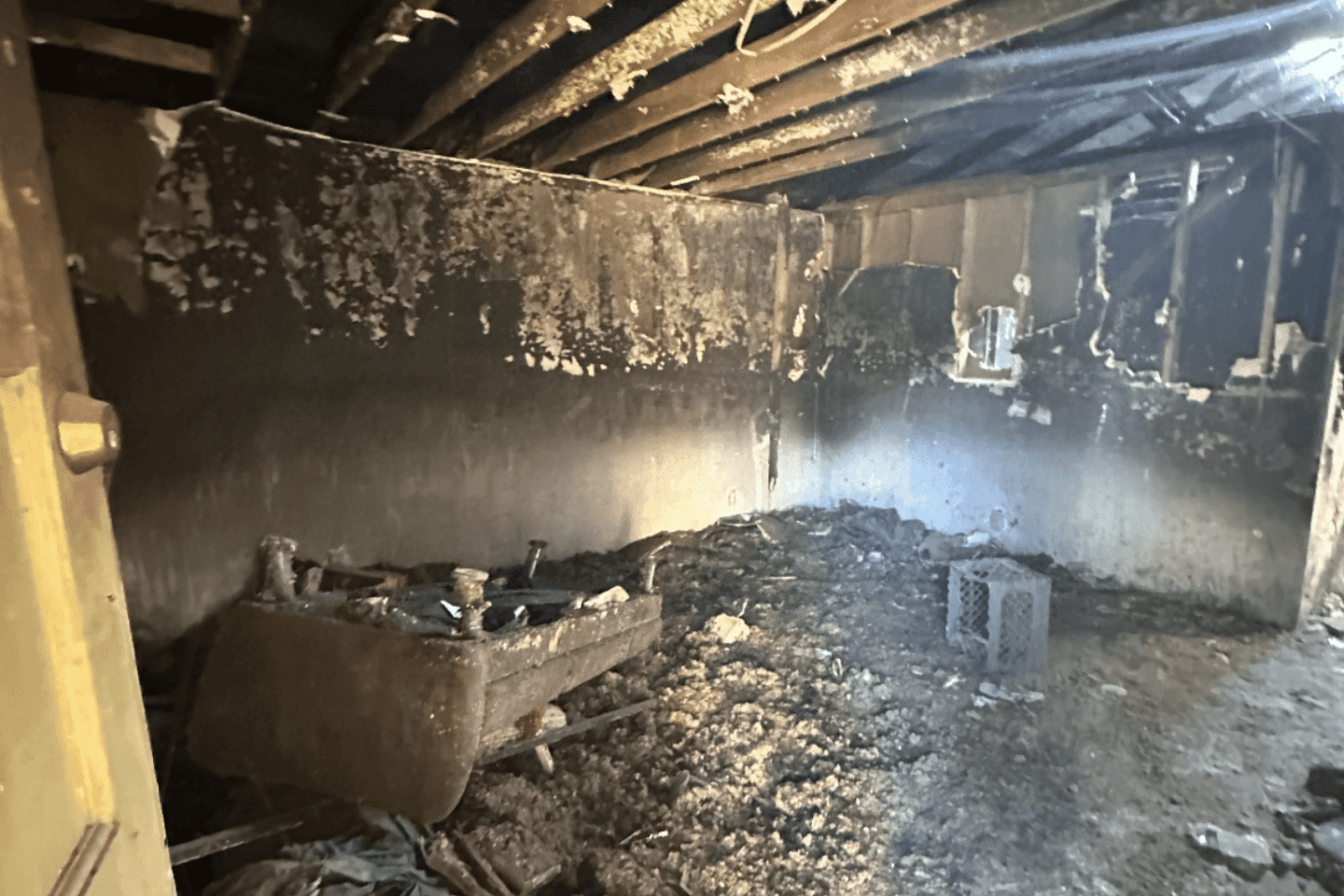 Room with severe fire damage; walls and ceiling are blackened, debris and charred remains of furniture cover the floor.